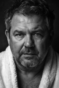 Amateur photo Low quality: dutch 58yo chubby male , wearing white robe, very short black grey hair, hairy, looking seductive. Upperbody photo.
