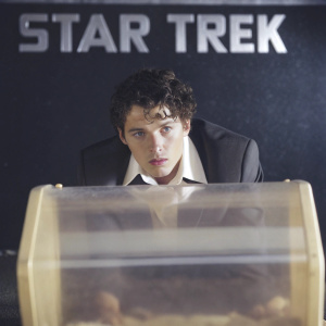 Anton Yelchin at the Star Trek premiere. Wears black suit, white shirt. Bold white text on black background. Focused on face and upper body, with serious expression.