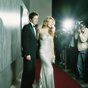 Topher Grace and Ashley Hinshaw attending a glamorous award show. Lavish red carpet and a backdrop filled with paparazzi and flashing lights.
