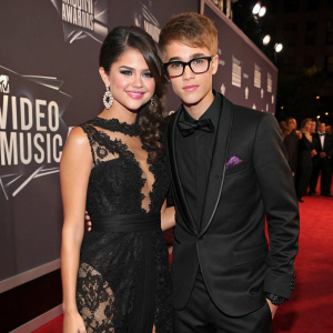 Selena Gomez and Justin Bieber attending the MTV Video Music Awards. Both dressed in formal attire, Justin in a black suit with glasses, Selena in an elegant black lace dress.