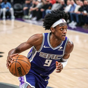 De'Aaron Fox, intense look, in action during NBA game. Sporty attire, Kings jersey. Court background, crowd blurred.