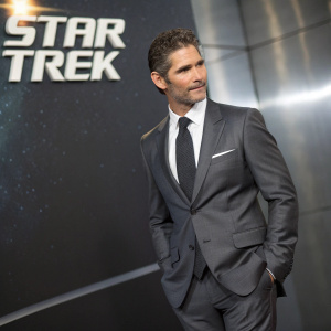 Eric Bana in a sleek grey suit, dark tie, and white shirt, standing confidently. Dark backdrop with glowing Star Trek logo. Soft lighting highlights his sharp features.
