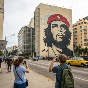 Large mural of Che Guevara painted on the side of a building in a vibrant city street. Tourists taking photos in front of the mural.