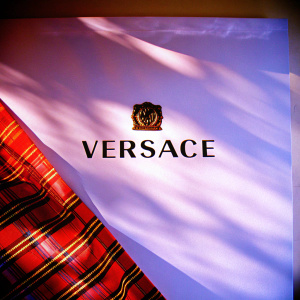 Design concept for Versace's winter collection. Bold black 'Versace' logo on bright white backdrop. Intricate plaid pattern on red fabric