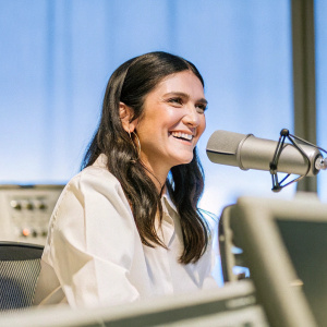 Nina Dobrev, seated at a microphone, smiling warmly. SiriusXM studios background. Audio equipment visible