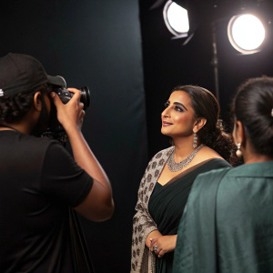 Vidya Balan, Bollywood star, mid-photo shoot. Dark studio setting. Photographer and assistants in frame. Candid moment.