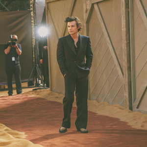 Harry Styles, dressed in a sharp black suit, at the 'Dunkirk' premiere in NYC. Standing in front of a red carpet with flashing cameras.