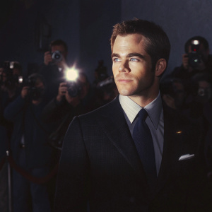 Chris Pine at the premiere. Wearing black suit with deep blue tie. Red carpet event. Surrounded by flashing cameras.