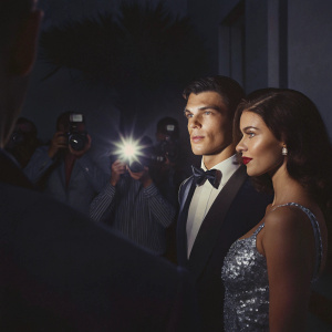 Finn Wittrock and Sarah Roberts at a Hollywood premiere. Wittrock in a tuxedo, Roberts in a silver sequined gown. Bright lights and paparazzi in background.