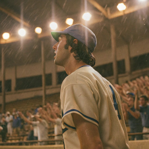 Randal Grichuk, baseball player, in a white jersey with blue accents. Stadium lights flickering. Crowd cheering in the background.