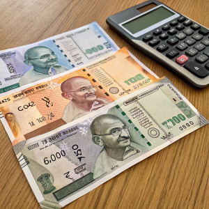 Various Indian currency notes with Mahatma Gandhi's image, laid out on a wooden desk. Calculator beside the notes.