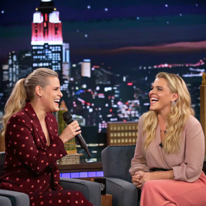 Jen Gotch and Busy Philipps on stage during a talk show. The background features a bustling cityscape.
