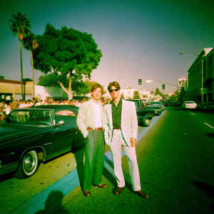 Vintage photo of Tom Cruise and Val Kilmer at the Top Gun premiere. Black and white, grainy texture. Background: bustling city street with classic cars