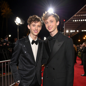 Troye Sivan and Sage Sivan, siblings, at the annual Grammy Awards ceremony. Dressed in elegant attire, posing for the cameras. Nighttime event with spotlighted stage.