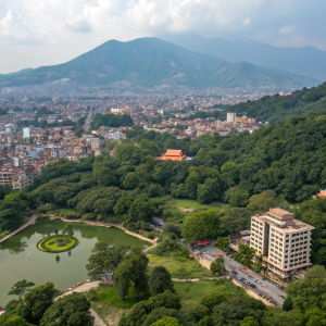 Bird's eye view of Kathmandu, Nepal. The cityscape is a mix of modern and traditional architecture. Green parks and ponds are scattered amidst the bustling urban environment. Hilly terrain provides a natural backdrop.