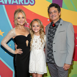 Barbara Alyn Woods, Alyvia Alyn Woods, Don Mancini, and Zackary Arthur at an awards show. Barbara in black dress, Alyvia in white lace, Don in patterned shirt and gray blazer, Zackary in tuxedo. Bold, colorful backdrop.