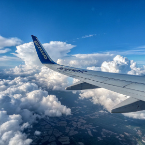 Photograph of a wing of an aircraft with the Ryanair logo visible. Clear blue sky, clouds in the background