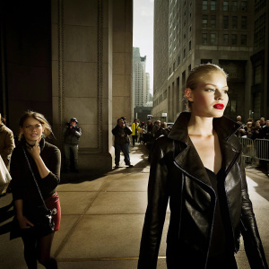 Nicki Minaj, in a black leather jacket and bold red lipstick, walking down a busy street during New York Fashion Week.