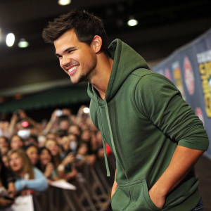 Taylor Lautner, wearing a green hoodie, hanging out at a Comic-Con event. Crowds of excited fans in the background
