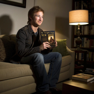 Actor Michael Welch, holding 'The Twilight Saga: New Moon' DVD, in a cozy living room setting. A dimly lit corner with soft shadows