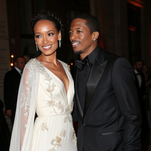 Selita Ebanks and Nick Cannon at a glamorous gala. Ebanks in elegant white gown with delicate embroidery, posing gracefully. Cannon in sleek black tuxedo, beaming with warmth. Dim lighting casts soft shadows, highlighting their attire and faces