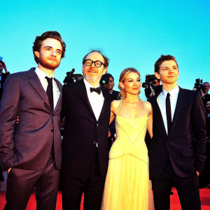 Robert Pattinson, Sienna Miller, James Gray, and Tom Holland at the BAFTA Film Awards. Black tie event, standing close together, against red carpet backdrop with flashing cameras