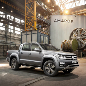 Digital rendering of a gray Volkswagen Amarok SUV amidst industrial machinery. Background features large metallic components and mechanical parts. Sign reads 'AMAROK'