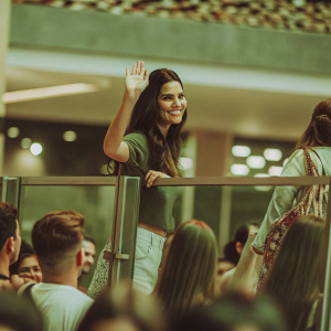 Adriana Lima at a mall grand opening event, waving to the crowd. She's wearing a casual outfit, smiling brightly.