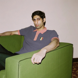 Photograph of Ashish Nehra, Indian cricketer. Formal attire, navy blue polo with orange trim and national crest. India logo visible. Quiet, neutral background. Event photo.