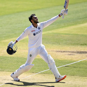 Axar Patel, cricketer, in action pose, wearing all white uniform with sponsor logos. Cricket ground background, sunny day.