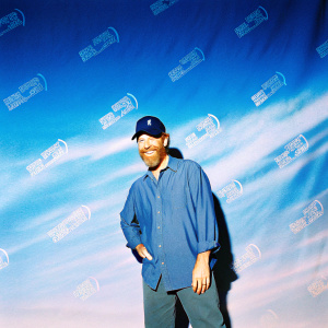 J.K. Simmons, Caucasian actor, in casual blue shirt and D-cap. Friendly smile, full beard. Against vibrant backdrop with logos like Detroit Creativity Project and Laugh.