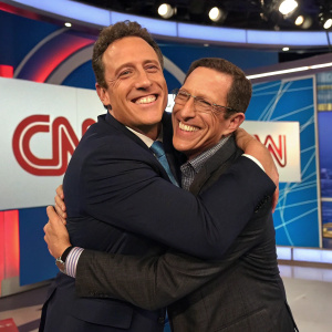Chris Cuomo and Richard Quest at CNN Studio. Hugging heartily in front of studio backdrop with network logo.