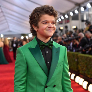 Gaten Matarazzo, the star of 'Stranger Things', at a glitzy gala. Wearing a vibrant green blazer. Flashing crowd in the background.