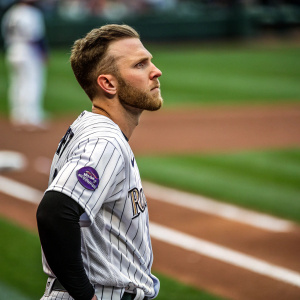 Close-up of Trevor Story, intense gaze, standing alone on a baseball diamond. Green field blurred in background