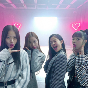 BLACKPINK members in a candid photo shoot. Various hairstyles and playful expressions. Neon pink studio backdrop with heart symbol.