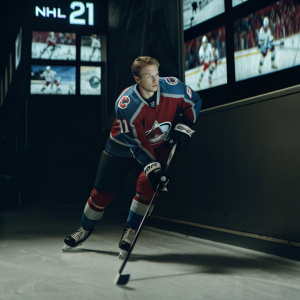 Nathan MacKinnon, star player, showcased in vibrant promo for NHL 21. Set amidst a lively montage of hockey action and branding elements. Dynamic pose highlights his athletic prowess.