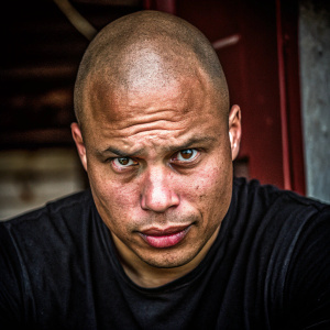Close-up photo of Cristiano Ronaldo. Bald, intense stare. Wearing plain black t-shirt. Dark background. Even lighting emphasizing facial features and shirt texture. Slightly turned gaze.