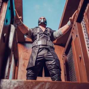 Highly detailed digital artwork featuring a strong supervillain, inspired by Bane, in an intense stance with hands spread wide. The villain wears a sleek, dark costume with metallic details and a defining belt. Set against a gritty, industrial backdrop bathed in dramatic lighting, the piece showcases intricate shading and texture to evoke realism and depth.