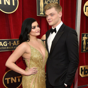 Ariel Winter and Levi Meaden at the SAG Awards. Wearing gold sequined dress and black tuxedo. Rich red velvet background with SAG-AFTRA logos