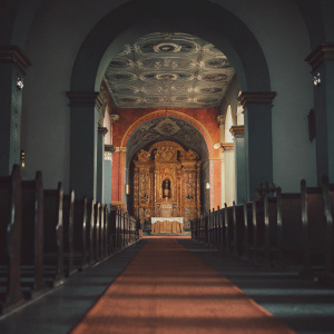 Immaculate Basilica of Huamanga Cathedral in Ayacucho, Peru. Long nave filled with ornate wooden pews and a vibrant rug. Golden altar and richly decorated columns and arches leading to the ceiling.