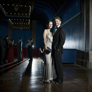 Tom Skerritt and Julie Tokashiki attending a gala event. Tom in a sleek black suit, Julie in a sophisticated beige gown.