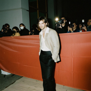 Nicholas Hoult at the gala, wearing a white shirt with black suit. Standing in front of a crowd, flashing cameras