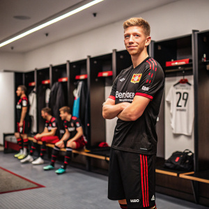 Mitchell Weiser, soccer player for Bayer 04 Leverkusen, posing in a locker room. Teammates in background.