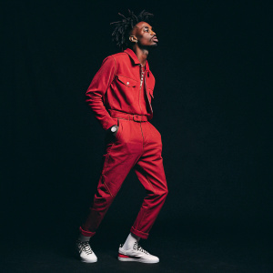 Playboi Carti, sporting a red outfit and dreadlocks, posing for his album cover 'Whole Lotta Red'. Black background