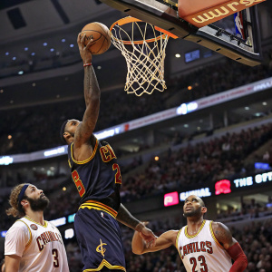 LeBron James mid-dunk with ball nearly touching the net. Background shows Joakim Noah and Carlos Boozer watching intently.