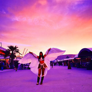 Ahri, a magical fox spirit, adorned in vibrant red and white attire with golden embellishments. Poses dramatically with wings spread wide. Set against a bustling fantasy marketplace.