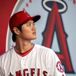 Close-up high-resolution image of Shohei Ohtani, Asian baseball player, dressed in a white Angels jersey with red piping. The iconic red 'A' logo prominently displayed in the background.