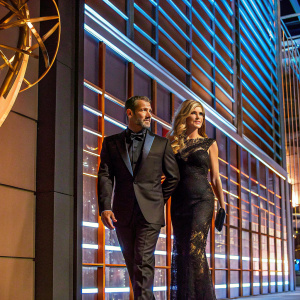 Antonio Banderas and Nicole Kimpel attending the 70th Primetime Emmy Awards. Antonio in sleek black suit. Nicole in elegant black lace gown. They pose against backdrop featuring NBC and Emmys logos.