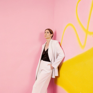 Jennifer Aniston in a candid photo shoot. Wearing a white blazer with a black blouse underneath. The background is a graffiti-covered wall.