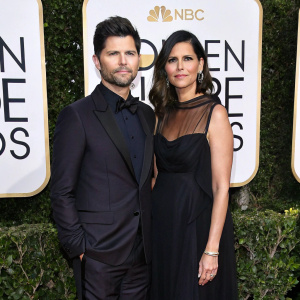 Adam Scott and Naomi Scott at the Golden Globe Awards. Dark suit, sleek black dress with sheer overlay. White backdrop with glitzy sponsor logos.